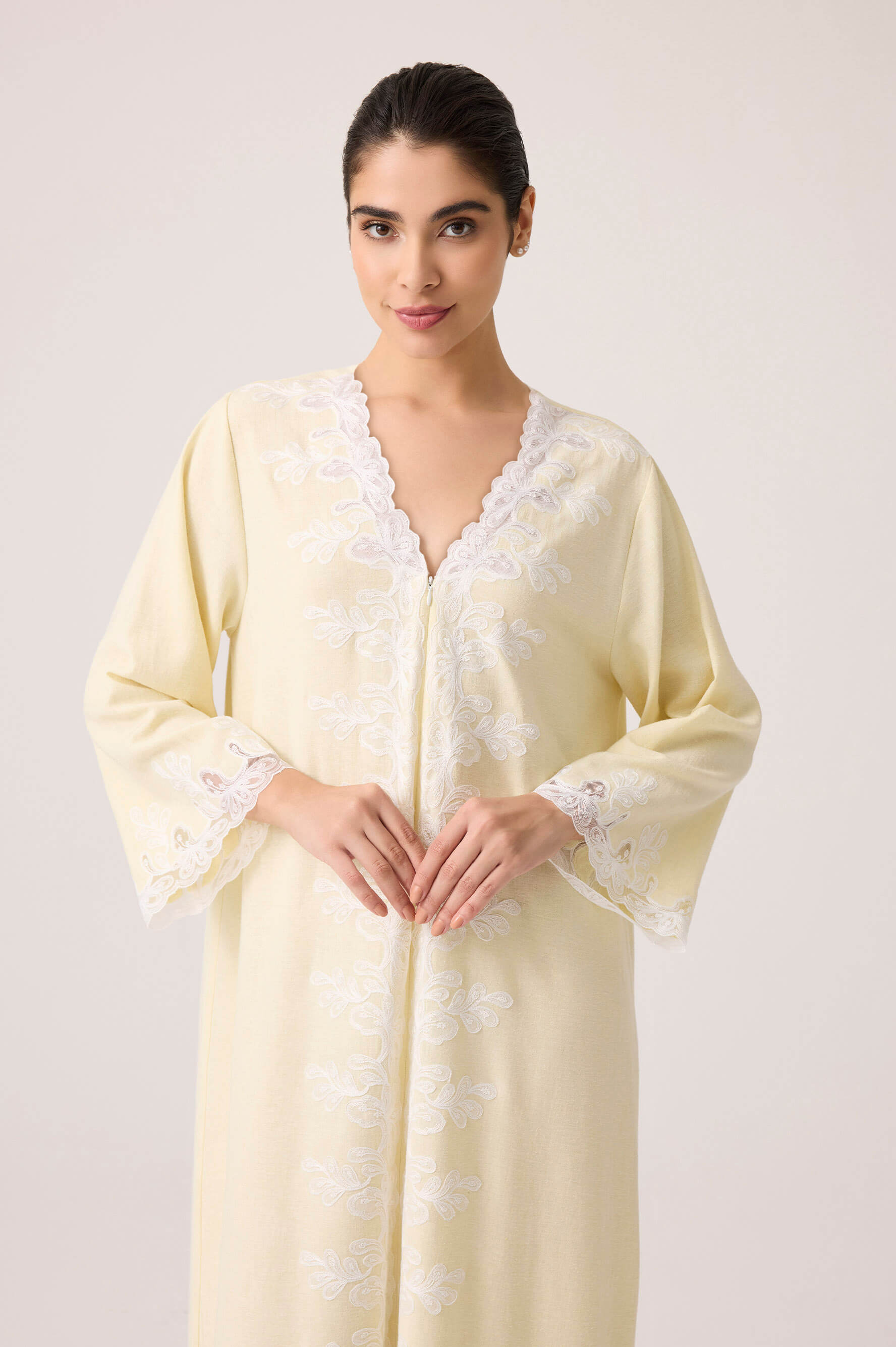 Woman wearing a light yellow nightgown with lace details on a white background