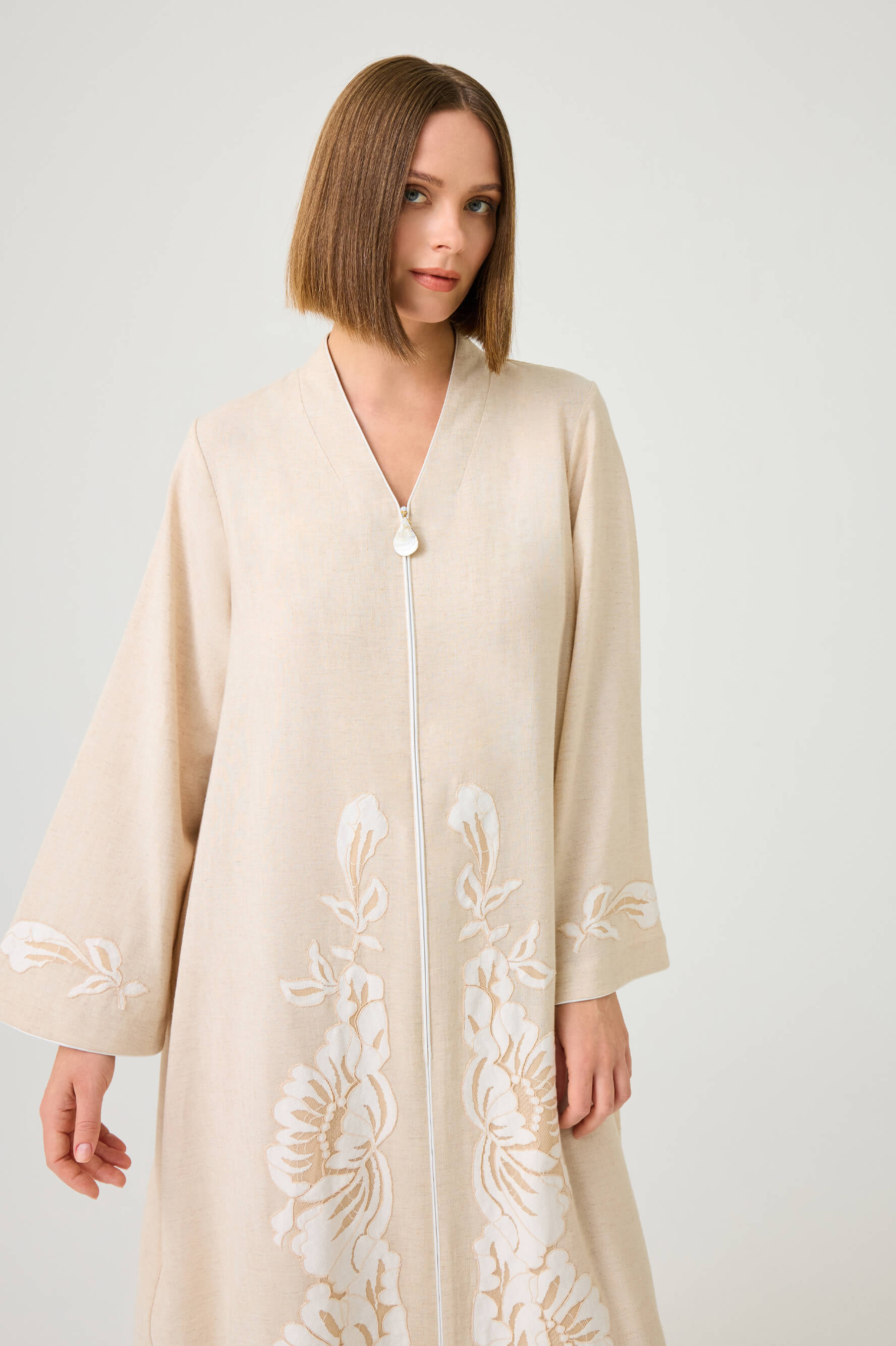 Woman wearing a beige embroidered dress against a white background