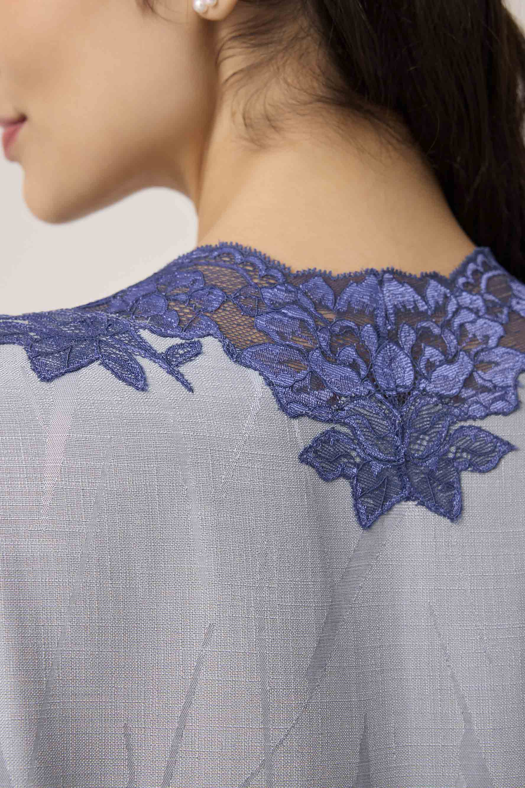 Close-up of a dress with blue lace detailing on a neutral background