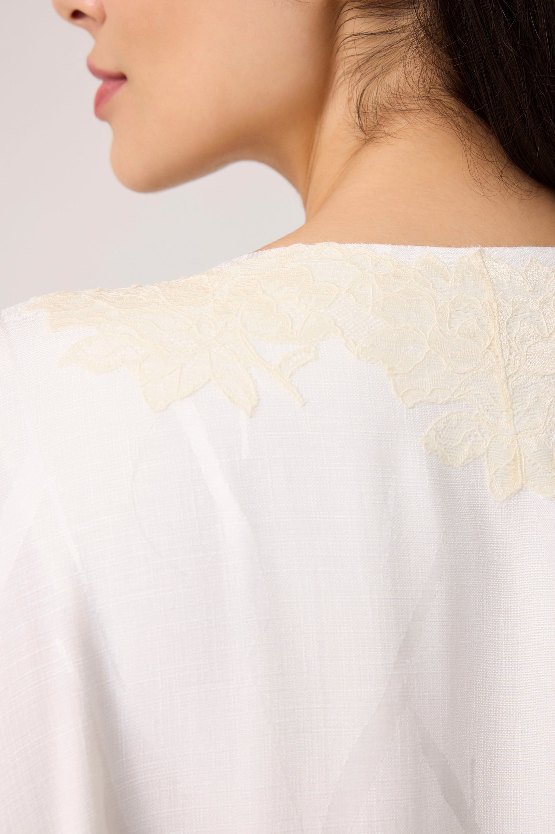 Close-up of a white garment with lace detailing on a neutral background