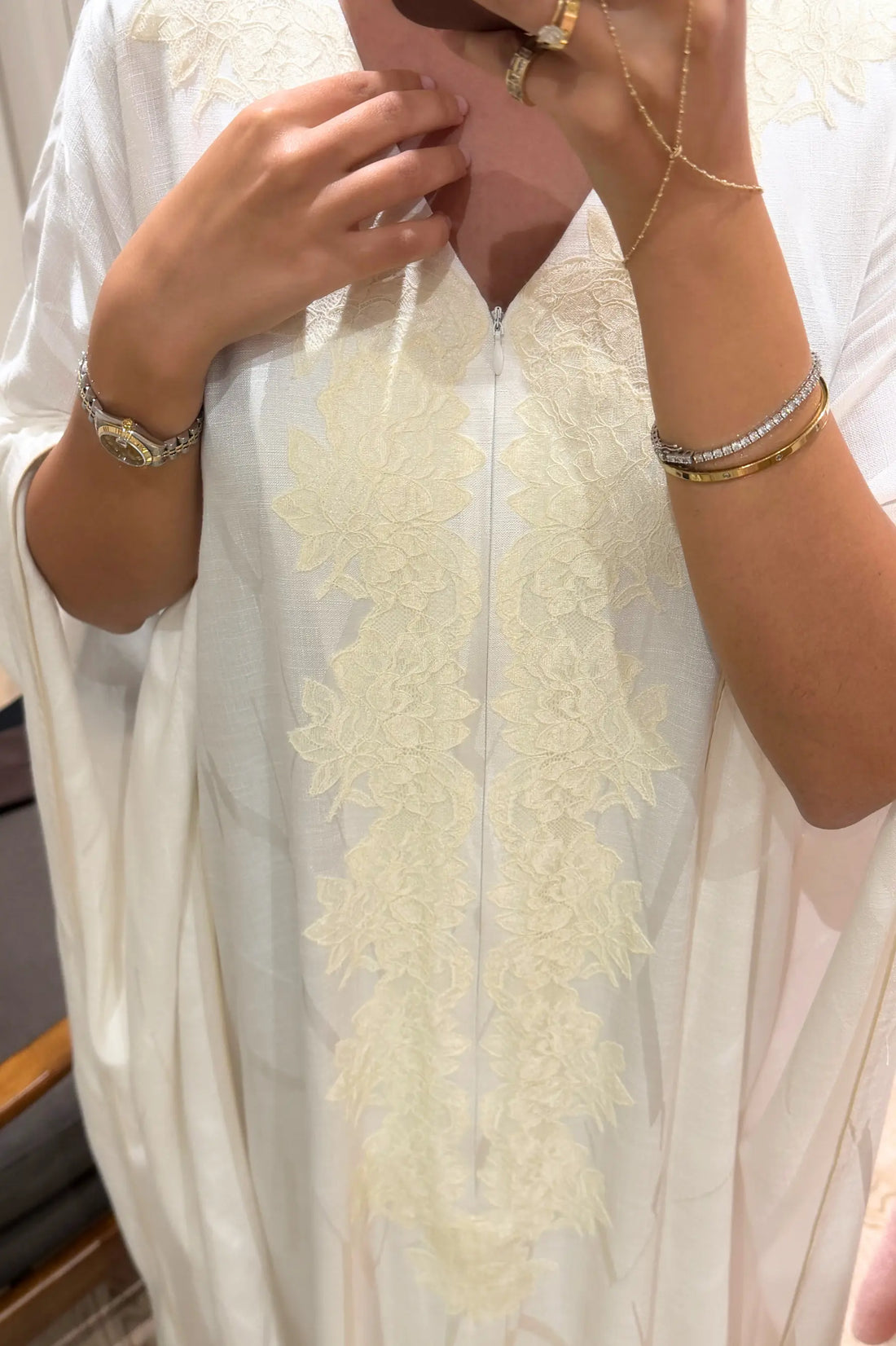 Close-up of a person wearing a white dress with floral embroidery and gold jewelry.