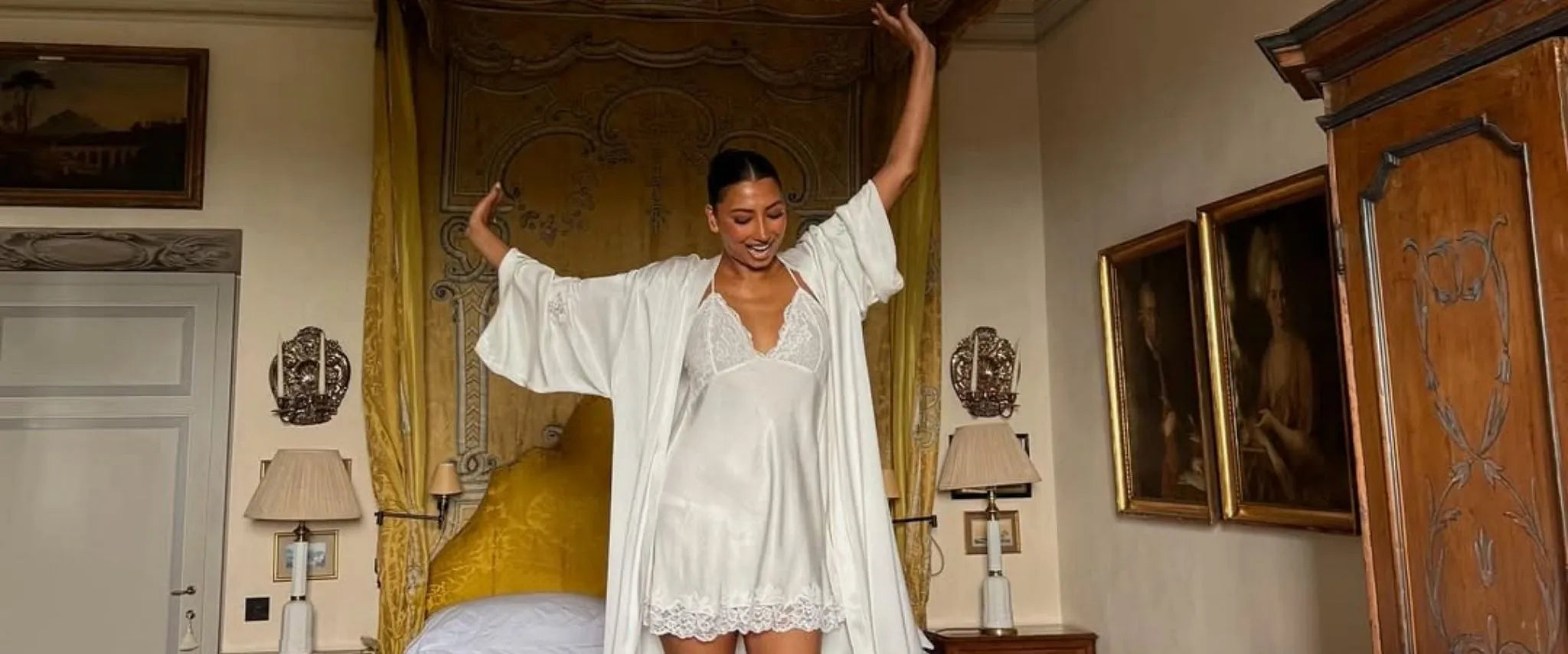 Woman in a white robe set standing in a bedroom with ornate decor