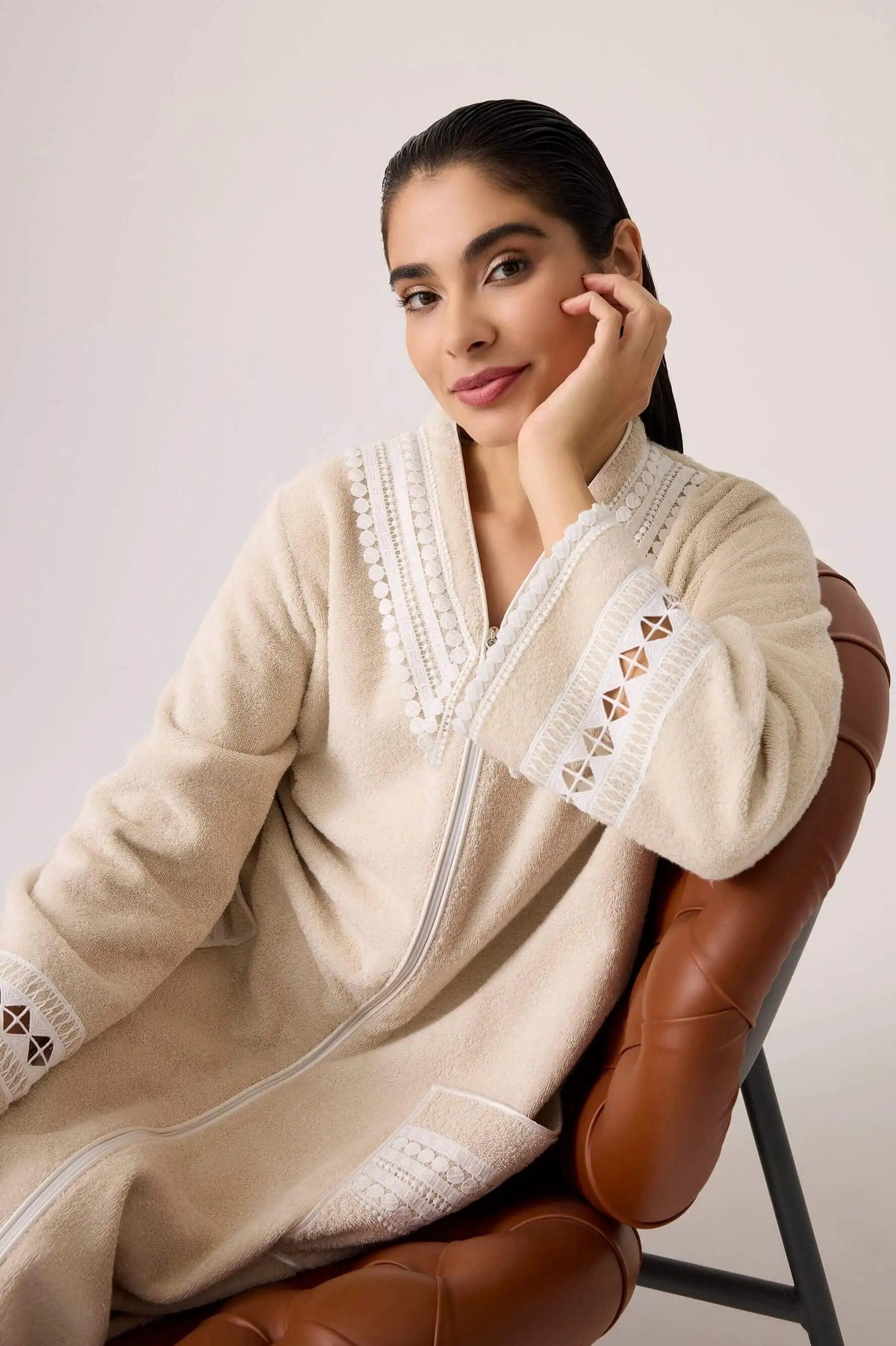 Model Woman wearing a beige bathrobe with lace details sitting on a brown chair.