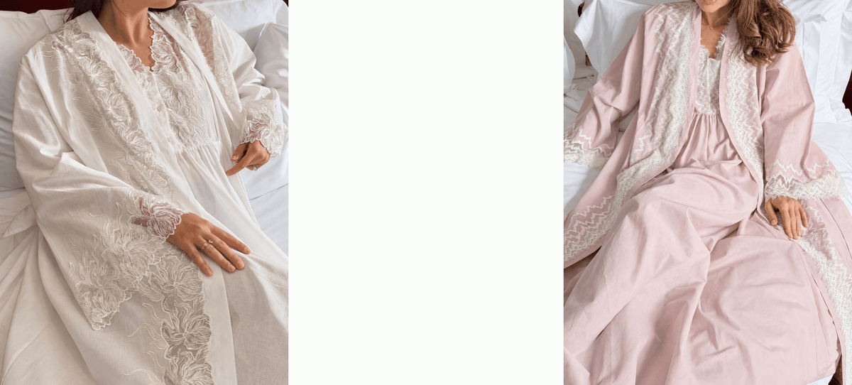 Two side-by-side views of a woman wearing a matching robe and nightgown set in two colors: one in white with cream lace trim, and the other in dusty pink with cream lace trim. Both are shown sitting on a white bed.