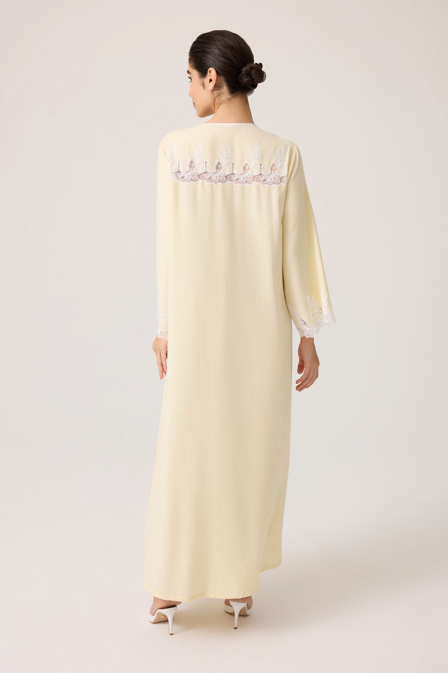 Woman wearing a long, light-colored dress with lace details on a white background