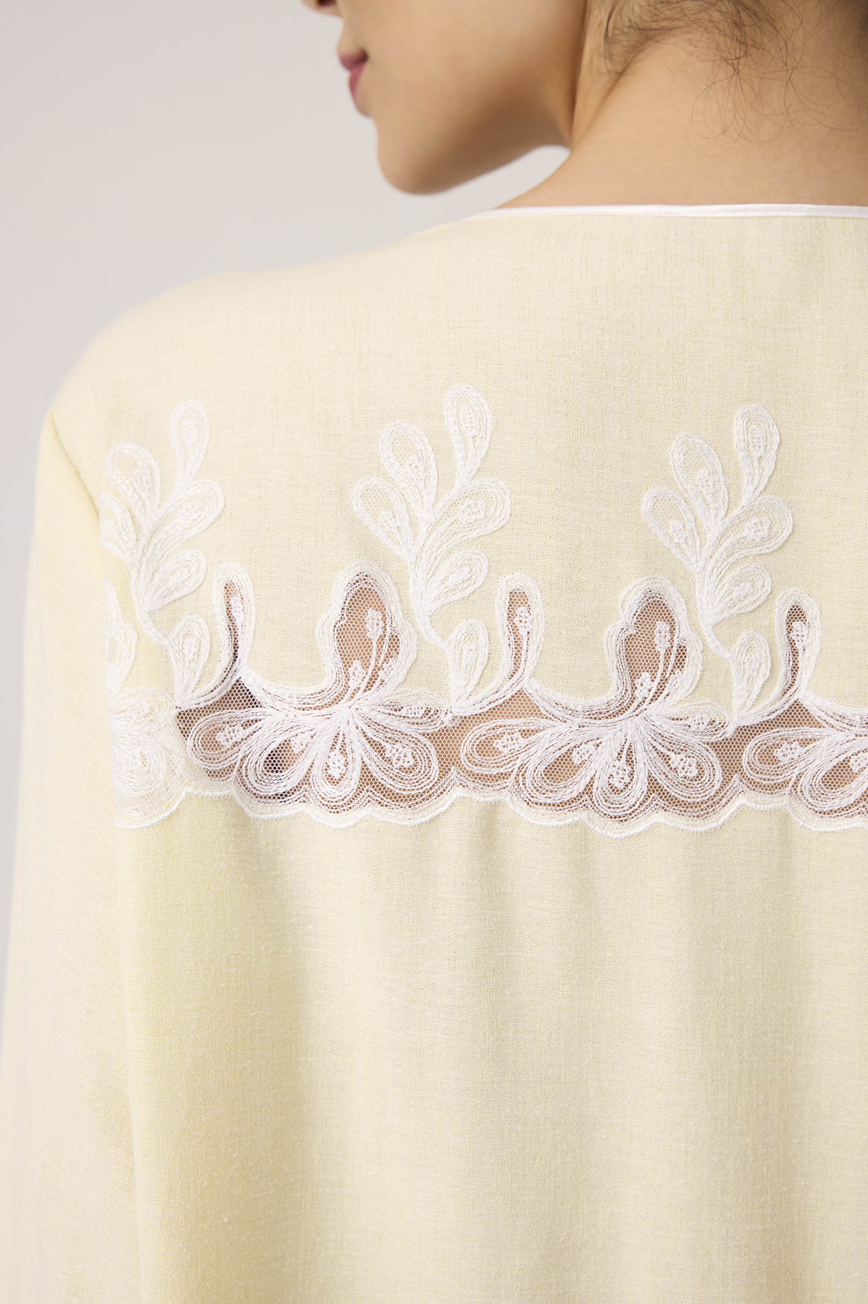 Close-up of a beige garment with intricate white lace detailing on a plain background