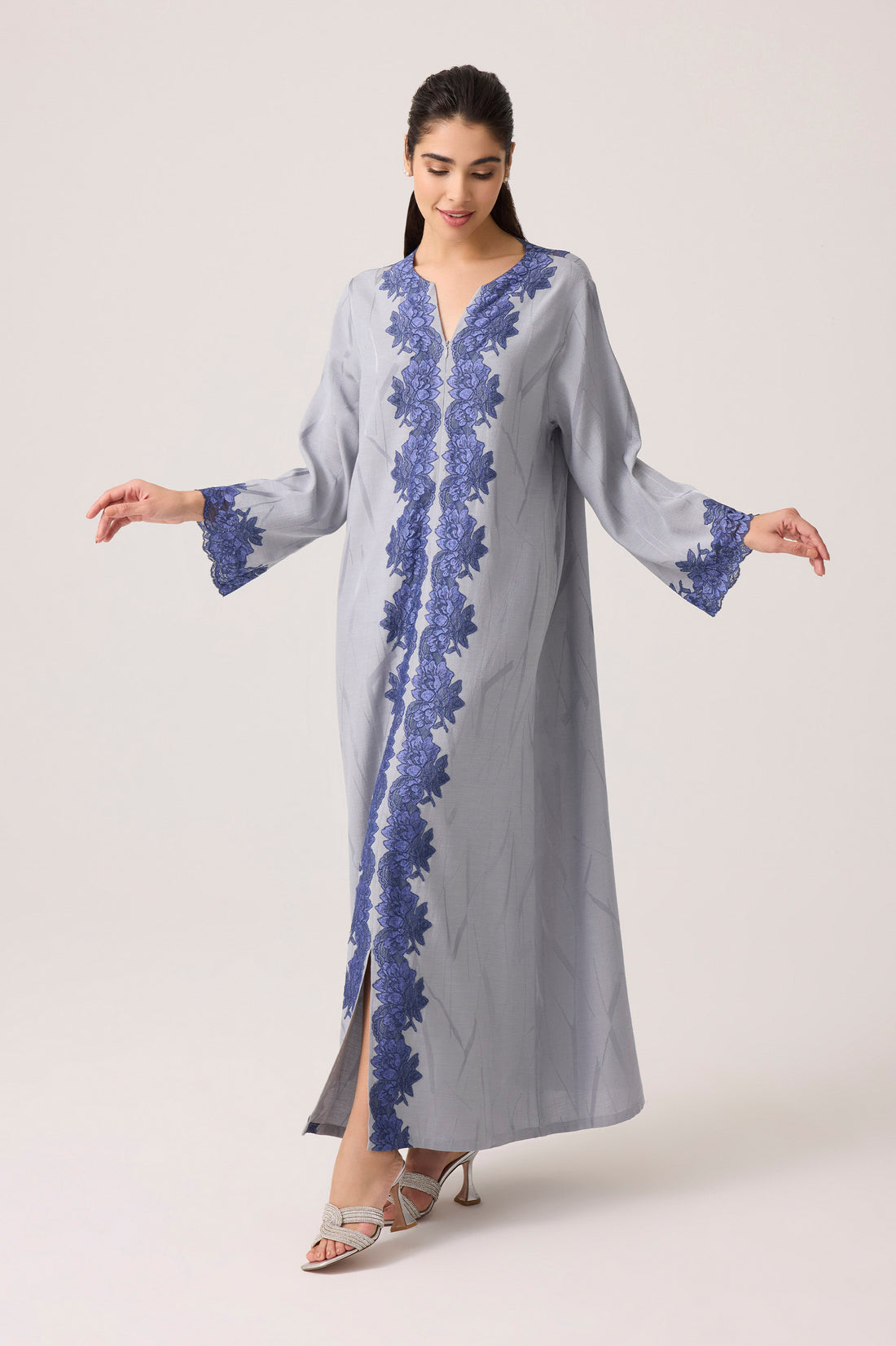Woman wearing a long, light gray dress with blue floral lace on a white background