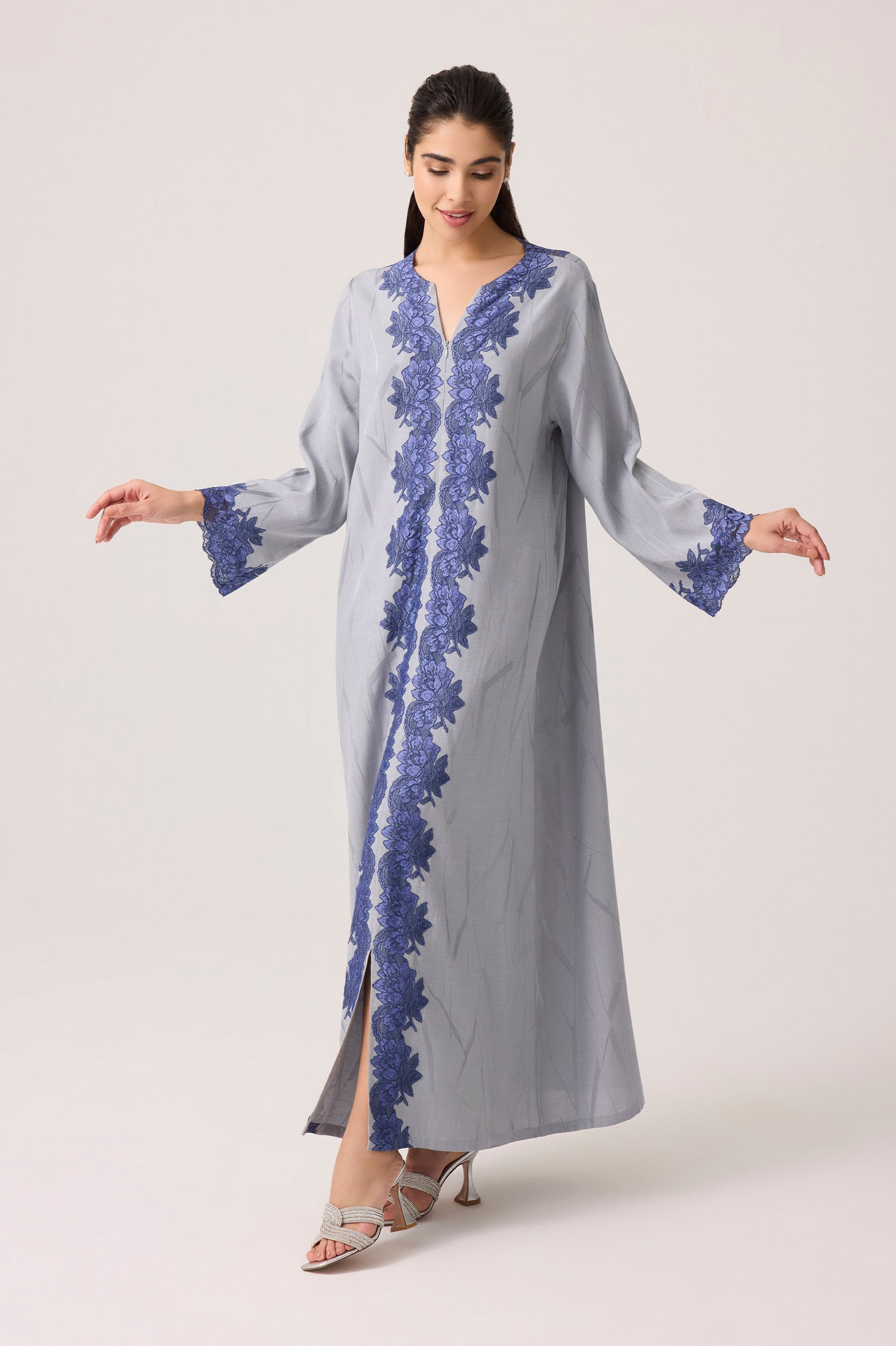 Woman wearing a long, light gray dress with blue floral lace on a white background