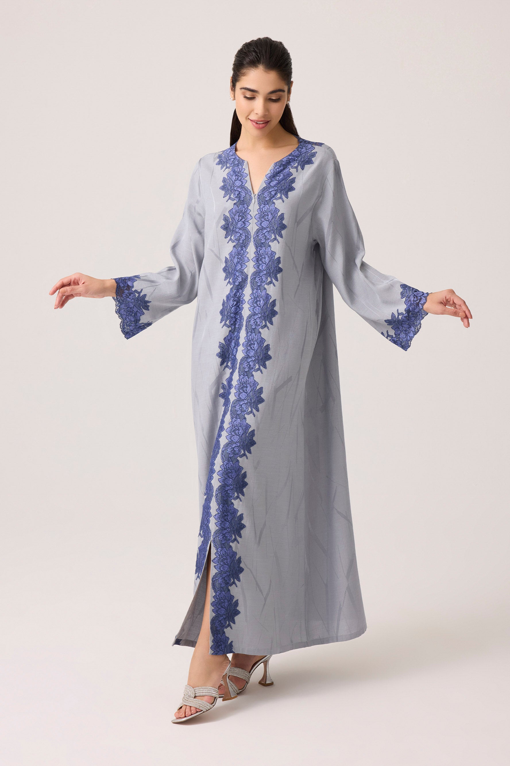 Woman wearing a long, light gray dress with blue floral lace on a white background