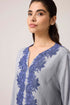 Woman wearing a light gray dress with blue lace details on a plain background