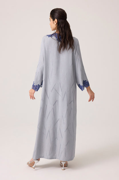 Woman wearing a long light gray dress with blue accents on a white background