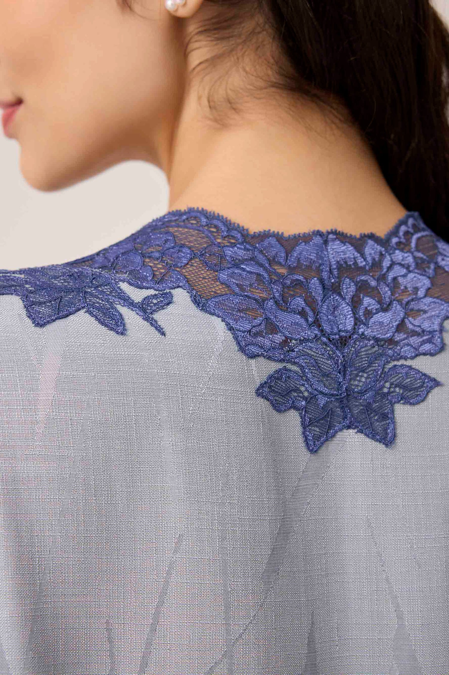 Close-up of a dress with blue lace detailing on a neutral background