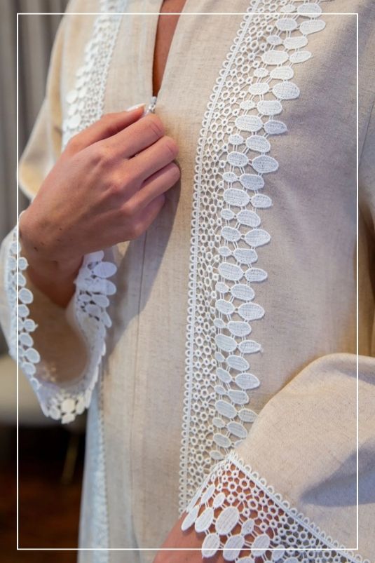 Woman wearing a light-colored dress with lace details in a softly blurred indoor setting.