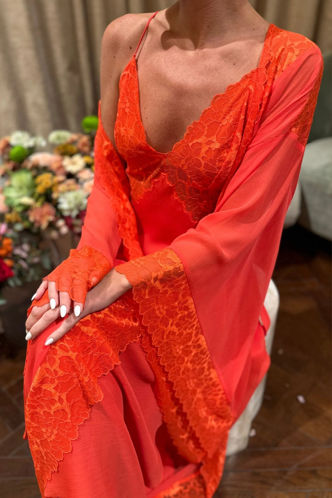 Lady wearing a bright orange lace dress with floral decorations in the background