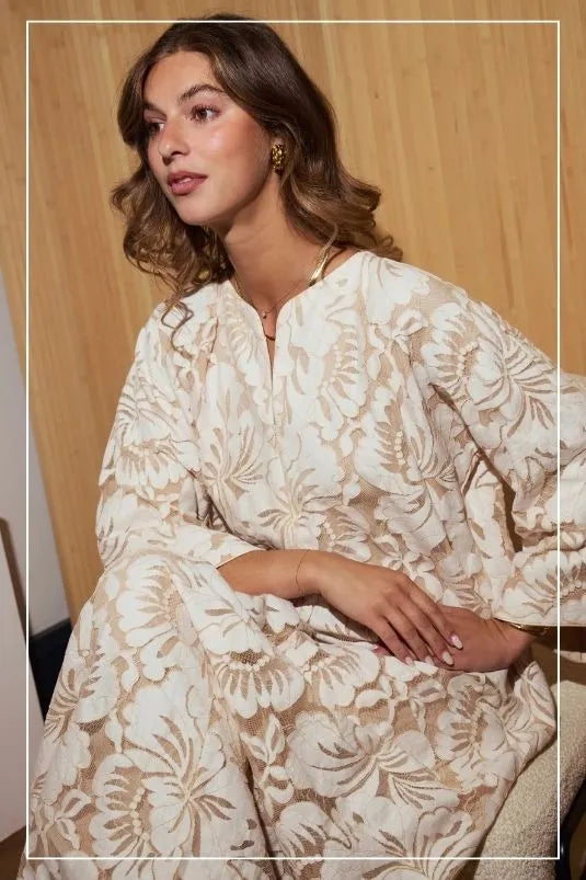 Woman wearing a beige zippered floral dress sitting against a wooden wall.