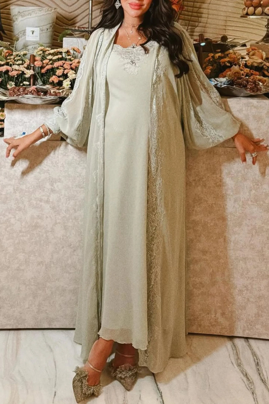 Woman in a light green dress with a matching robe standing in front of a floral arrangement.