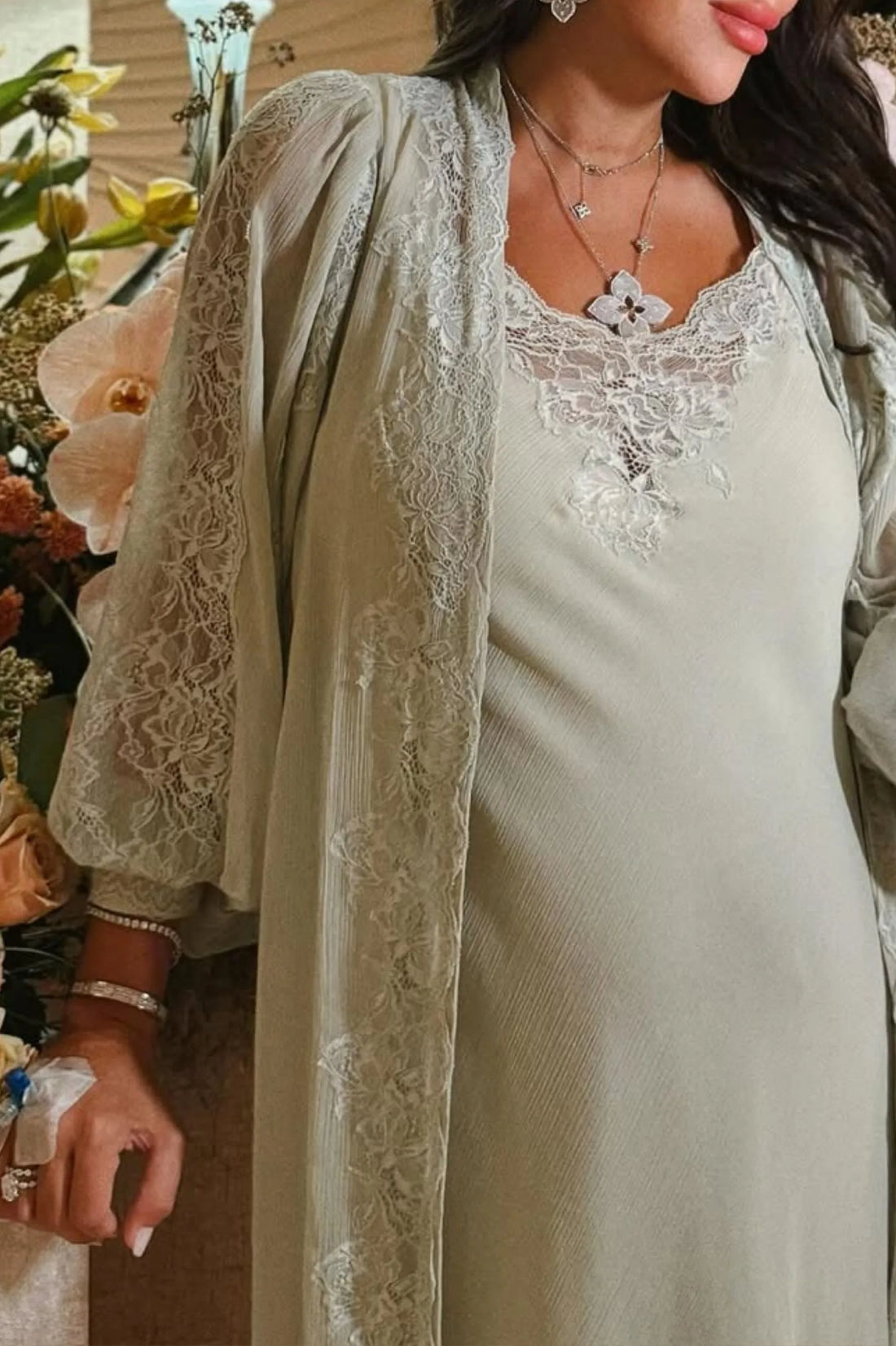 Woman wearing a light green colored lace dress nightgown with a matching robe, standing next to flowers.