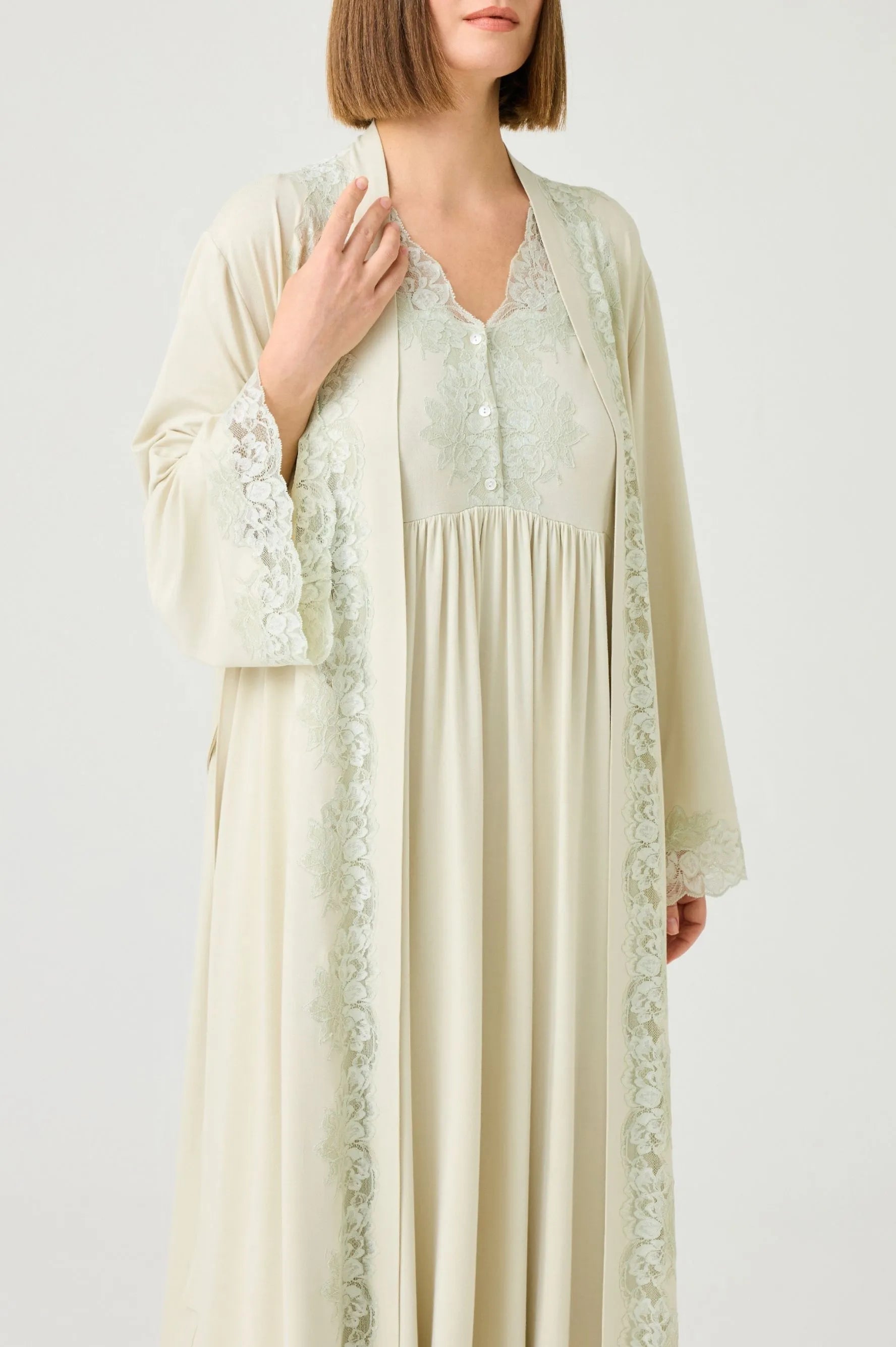 Woman wearing a long, green colored robe set with green lace details on a plain background